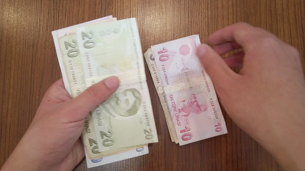 Teenager počítající náhodné množství bankovek turecké liry s portréty slavných tureckých osobností z oblasti vědy, literatury a hudby.