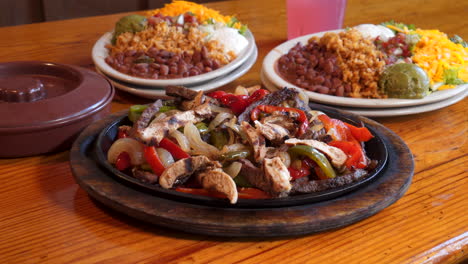 Hand-stabs-forkful-of-chicken-fajita-meat-from-skillet,-fixings-on-the-side,-close-up-pull-slide-slow-motion-4K