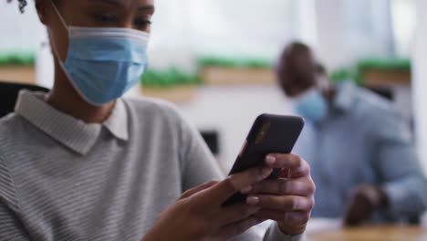 Diverse-male-and-female-business-colleagues-in-face-masks,-woman-using-smartphone-in-office