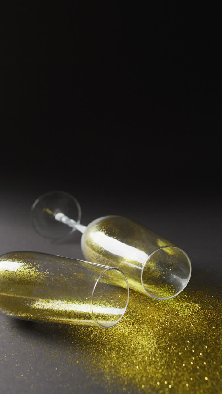 두 개의 떨어진 페인 플루트 컵의 수직 비디오가 금빛 반이는 것을 흘리고 있습니다.