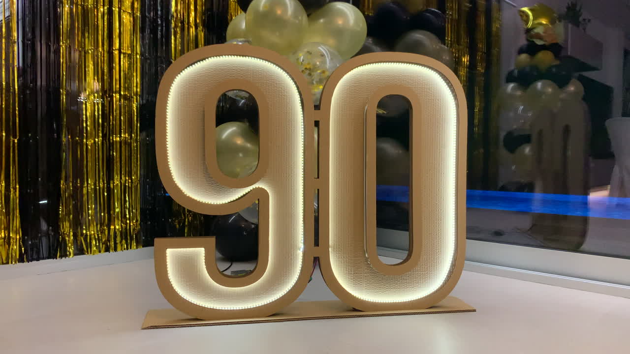símbolo de cartón del 90 aniversario con luces led con decoración negra y dorada en el fondo