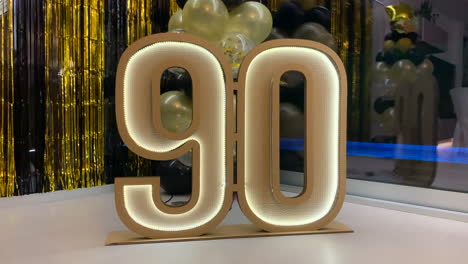 90th anniversary cardboard symbol with led lights with black and gold decoration in the background