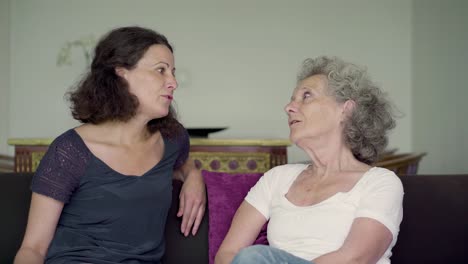 middle-aged daughter and mother talking on sofa, gesticulating