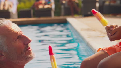 abuelo y nieto comiendo caramelos de hielo en el borde de la piscina en las vacaciones de verano de la familia