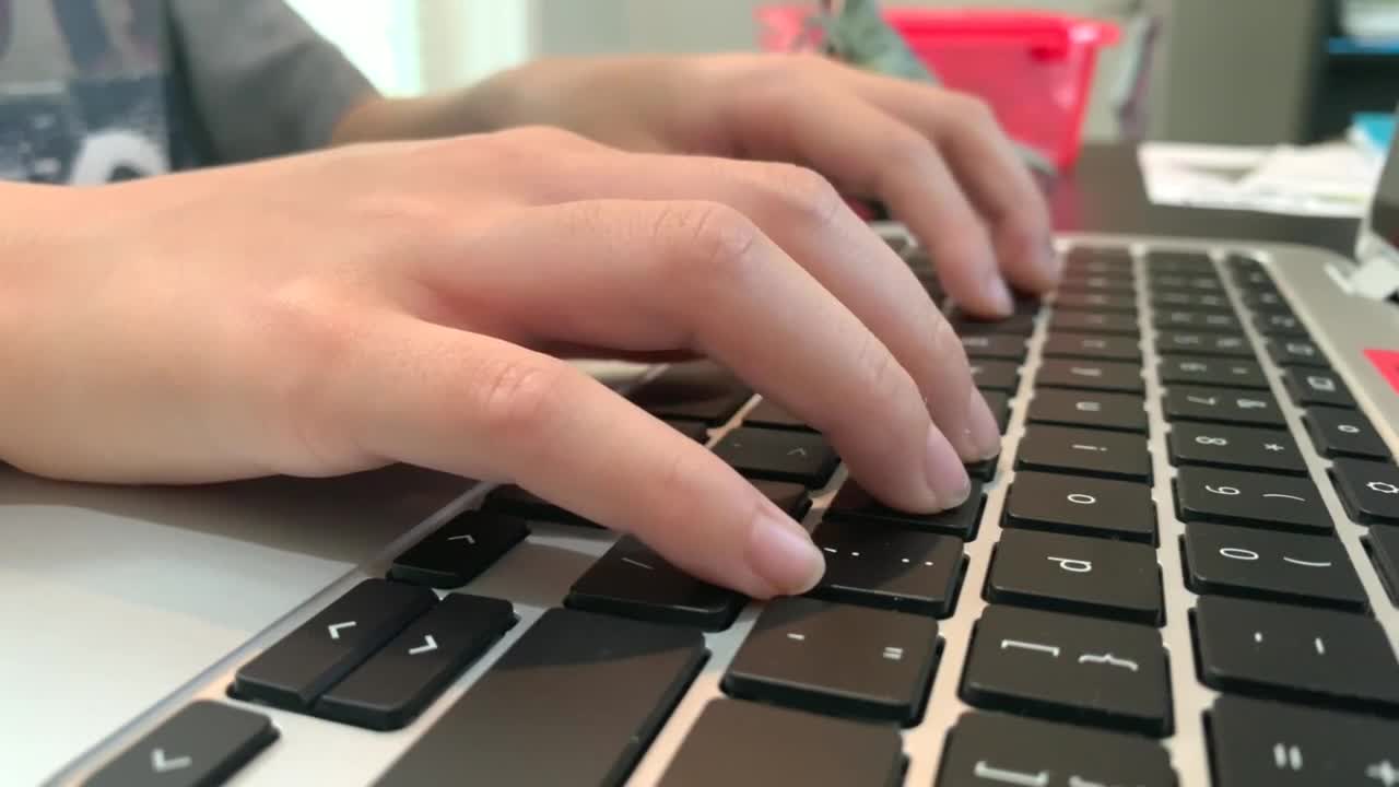Child hands typing on a Chromebook keyboard. Distance Learning. Online Education. Close-up on hands and keyboard. Side view in 4K.