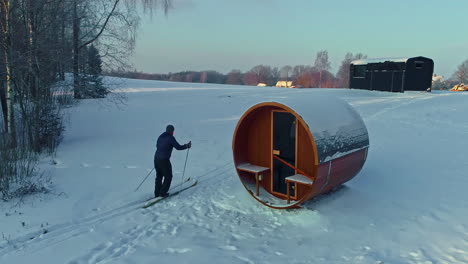 person on cross country skies skiing past a sauna and to a trailer cabin - aerial follow