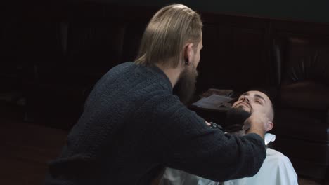barber trimming a man's beard with clippers in a barbershop