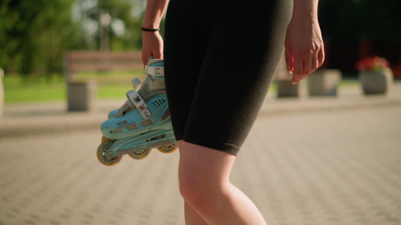 dama con medias negras caminando al aire libre mientras sostiene patines de color cian en su mano derecha, con un fondo borroso con bancos, vegetación exuberante y una olla de flores
