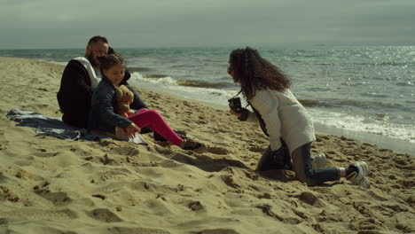 Sweet-family-enjoy-photosession-on-beach-sand.-Parent-kid-posing-picture-by-sea.