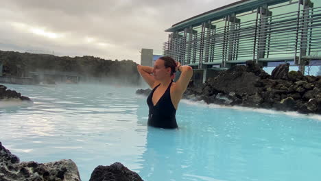 young girl in swimsuit making a ponytail in geothermal blue lagoon spa in iceland