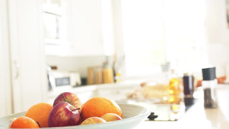 Obst-In-Einer-Schüssel-Und-Gewürze-Auf-Der-Theke-In-Einer-Sonnigen-Küche,-Zeitlupe