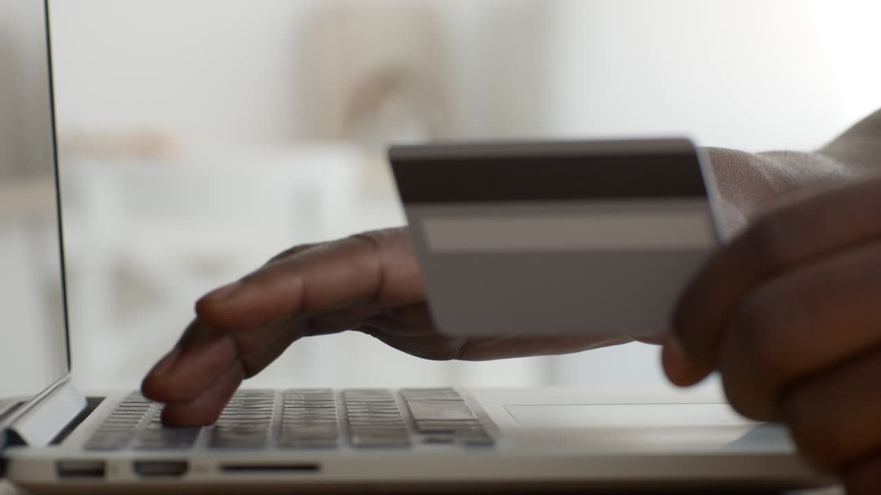 Online payment concept. Black man with credit card paying in internet, making order distantly, slow motion