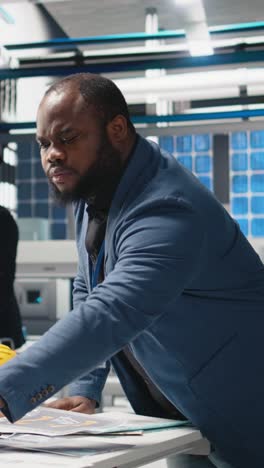 vertical video african american technician consulting performance metrics on papers and laptop