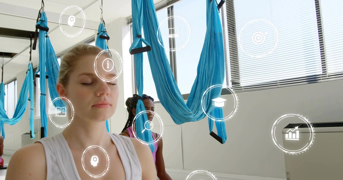 Duas mulheres meditando sob redes aéreas em estúdio de yoga, com ícones de aprendizado desaparecendo e câmera em movimento panorâmico.