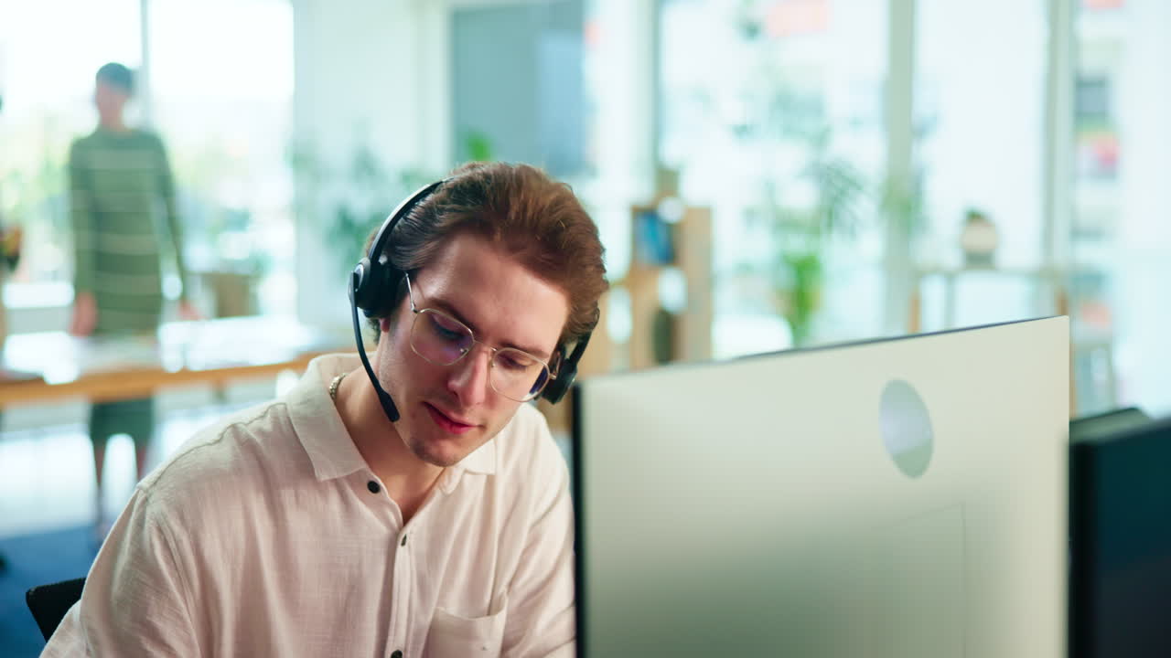 hombre trabajando en una computadora con auriculares en una oficina.