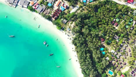 beautiful turquoise bay with calm clear water, anchored boats near white exotic beach and resort bungalows surrounded by palms, thailand