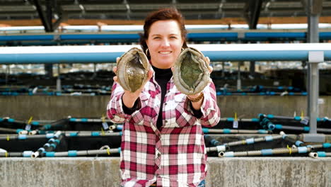 Woman-holds-up-two-adult-abalone-in-front-of-her,-South-Africa-aquaculture