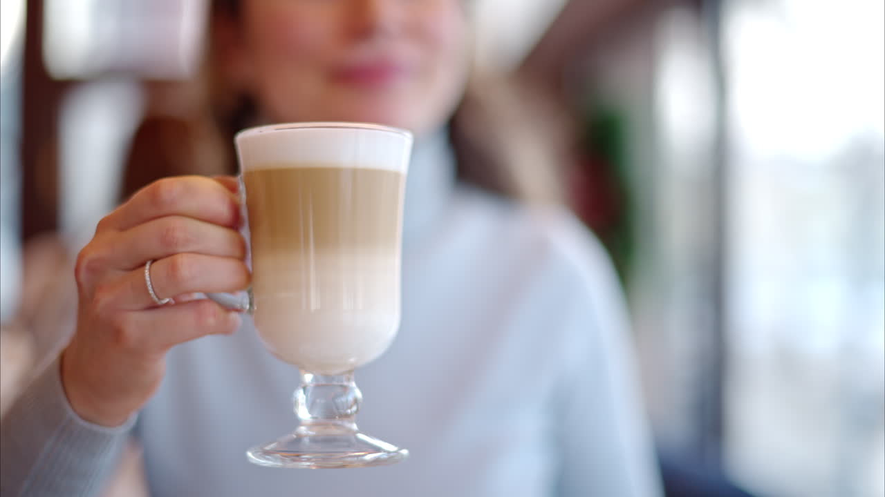 Happy woman drinking foamy latte in a restaurant. Glass transparent cup