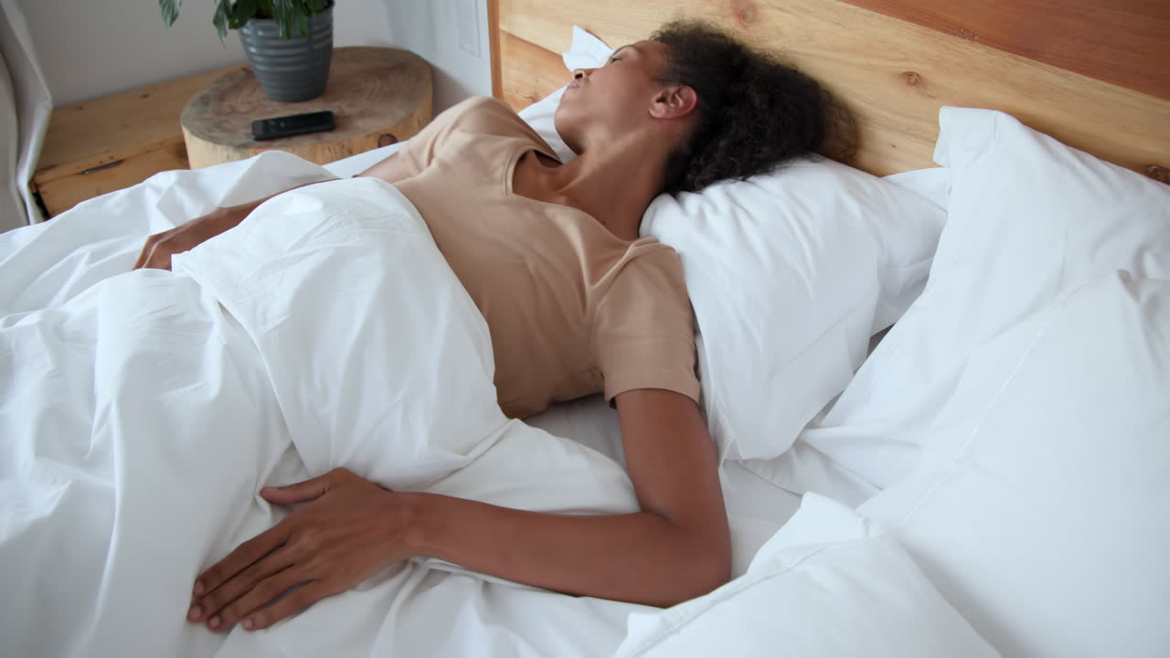 woman waking up in bed, stretching and looking relaxed at home