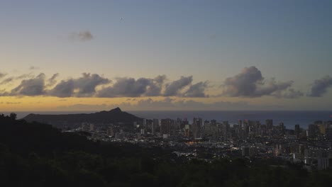 the city of honolulu at twilight from a view on a mountain as the sun reflects an orange alpenglow to the sky