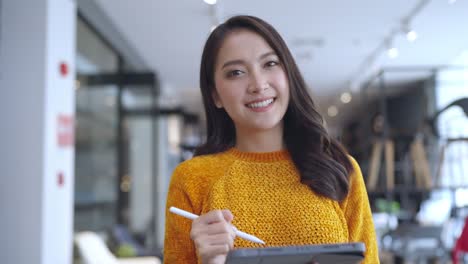 smart confidence asian female startup entrepreneur small business owner businesswoman wear smart casual cloth smile hand use tablet woking inventory checking in showroom office daytime background