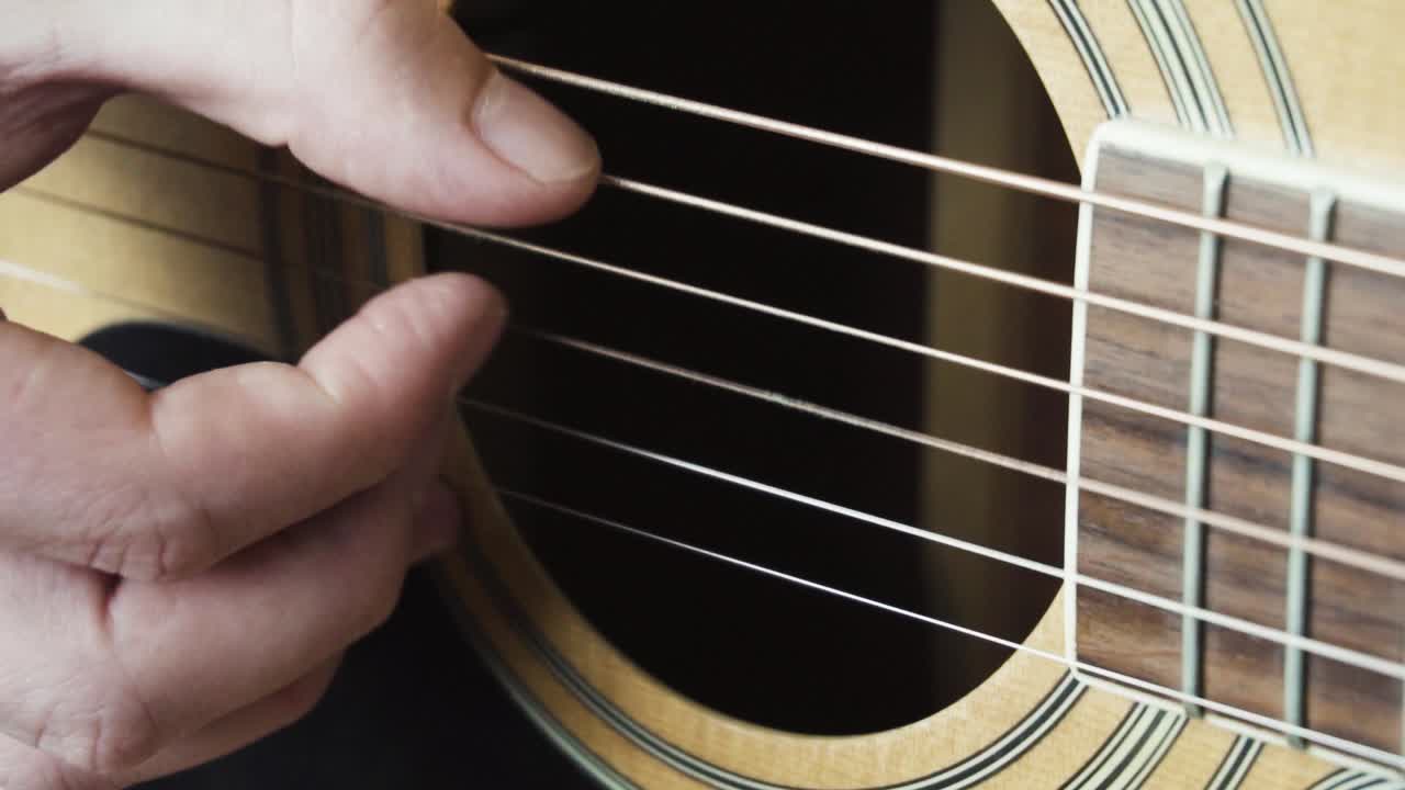 Slow motion close up static shot of a young man finger picking an Acoustic Guitar. (100fps)