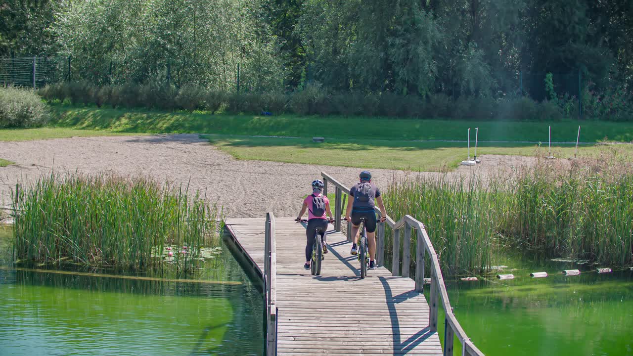 Par, der cykler på mountainbikes over træbro ved Radlje Ob Dravi Park i Slovenien. Følg skuddet