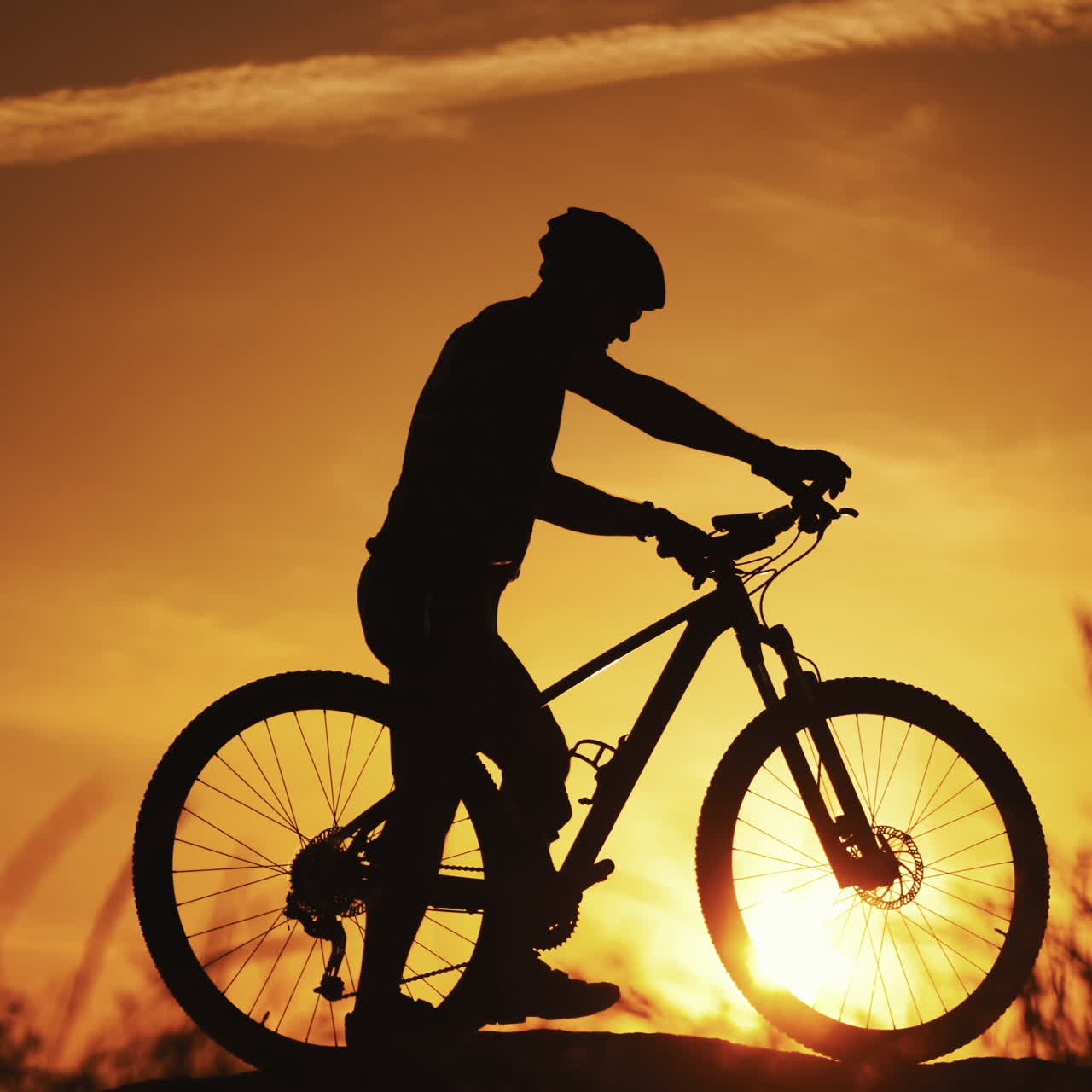 Silhouette of a biker with his bike walks outdoors at sunset. Healthy cyclist walking in the evening and a man's silhouette going by against the beautiful summer sunset.