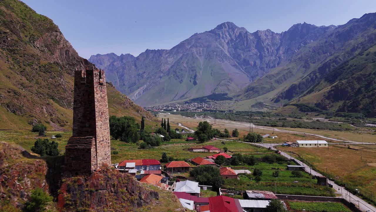 Historic tower in Kazbegi valley rural valley. Drone aerial fly past with mountainous valley and Georgian town in background