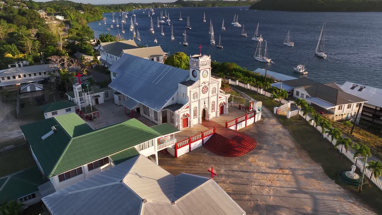Drone flyover historical church in Neiafu, Tonga to seaside with sailing boats during sunset.