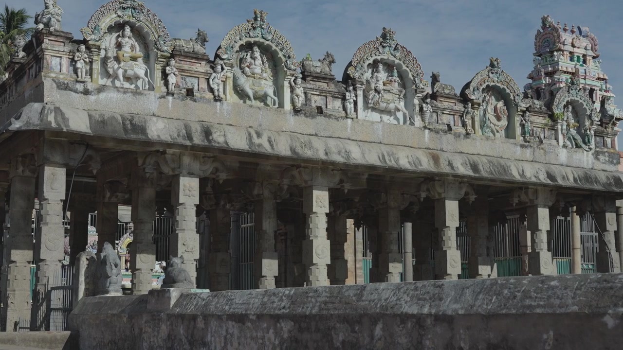 Ampia inquadratura di un antico mandapam in pietra con sculture ornate di divinità indù lungo il parapetto accanto alla vasca del tempio. Acqua sacra scintillante, pilastri intagliati, arte dravidica, Tamil Nadu, India del Sud