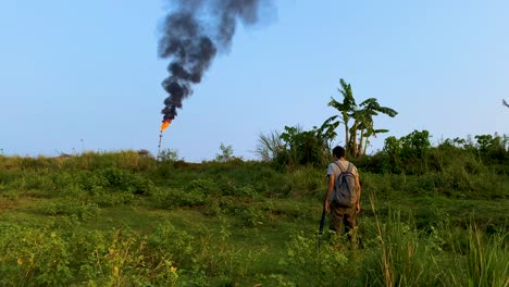 Environmental-Photographer-or-Reporter,-Shooting-pollution-scene-of-an-Oil-Refinery-Tower-in-Operation-which-is-Producing-a-Big-Flame-and-Dark-Fumes