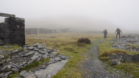 A-group-of-hikers-in-the-welsh-mountains-stopping-at-a-derelict-village-surrounded-by-mist