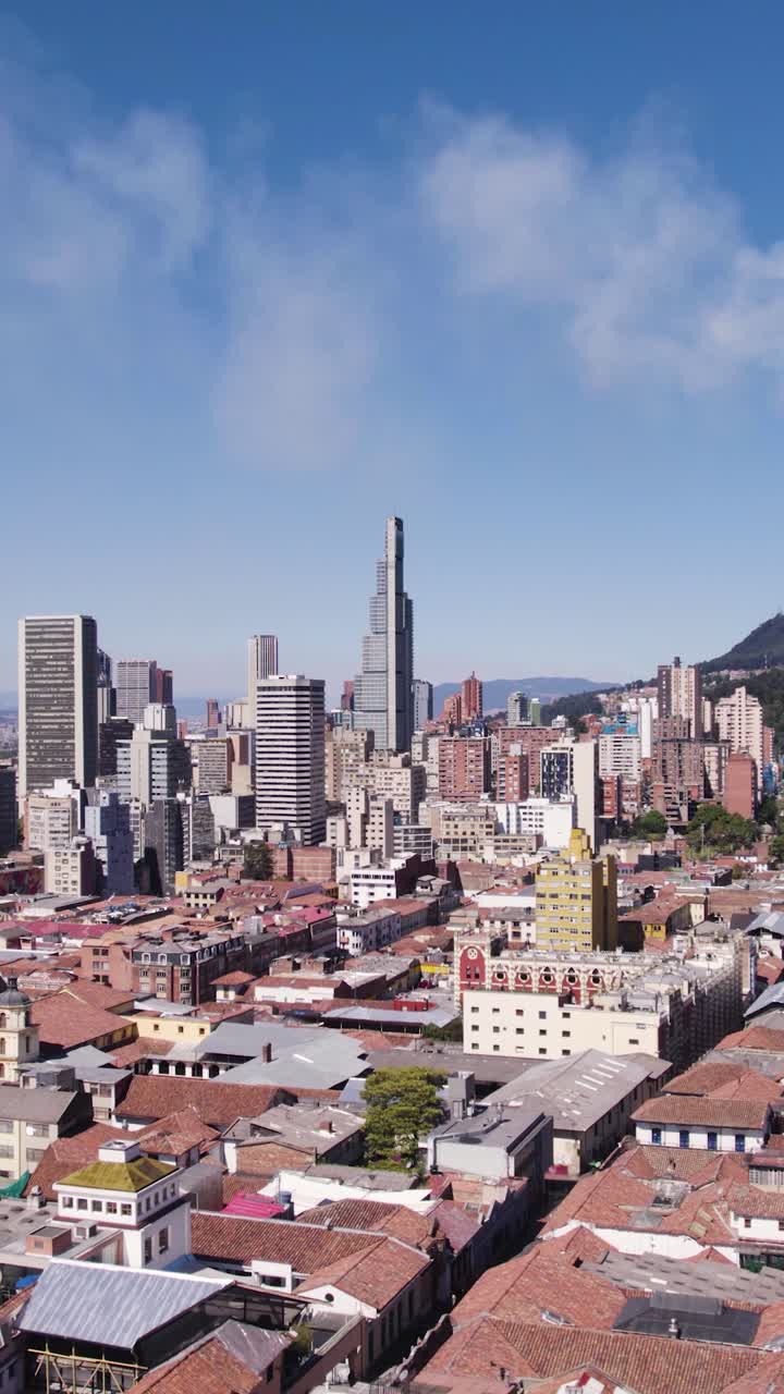 Aerial view of Bogota, Colombia, featuring a mix of modern skyscrapers and traditional buildings, set against a backdrop of mountains and blue sky. Vertical Video, Push Forward Shot