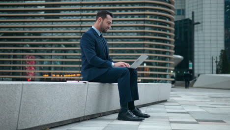 Businessman-working-on-laptop-computer-sitting-in-business-park-courtyard