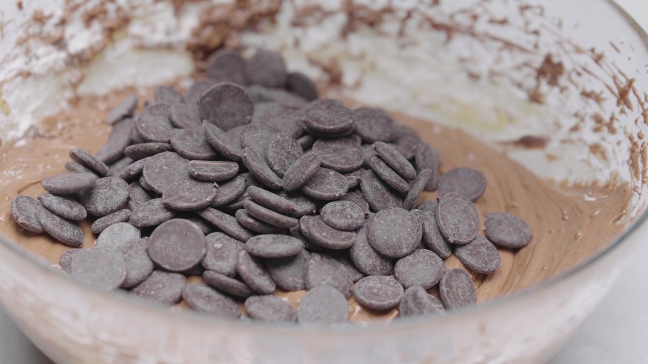 Close up of chocolate chips being poured into cookie dough in bowl during baking preparation