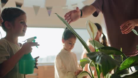 Una-Niña-De-Preescolar-Usa-Un-Rociador-Verde-Especial-Para-Rociar-Una-Flor-Con-Agua-Y-Regarla-Bajo-La-Atención-De-Su-Maestra.-Un-Hombre-Con-Una-Camiseta-Violeta-Durante-Un-Recreo-En-Un-Club-Para-Preparar-A-Los-Niños-Para-La-Escuela.