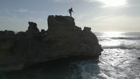 young man jumps off rocky cliff into the ocean, swims to shore