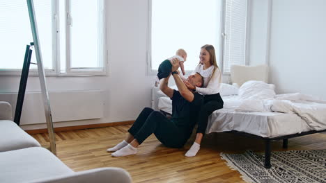 caucasian family together at home in their bedroom. smiling man raising his infant son above the head.