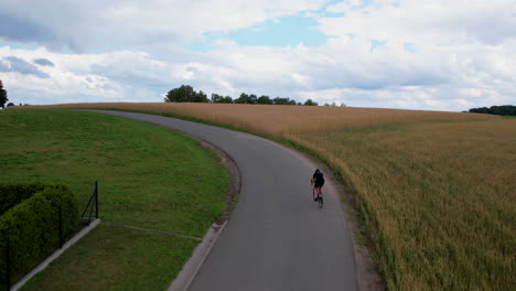 man biking on an uphill road along the field in the countryside