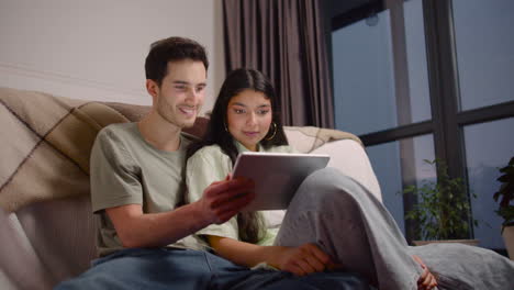 bottom view of couple watching comic movie on tablet while sitting on the floor at home 1