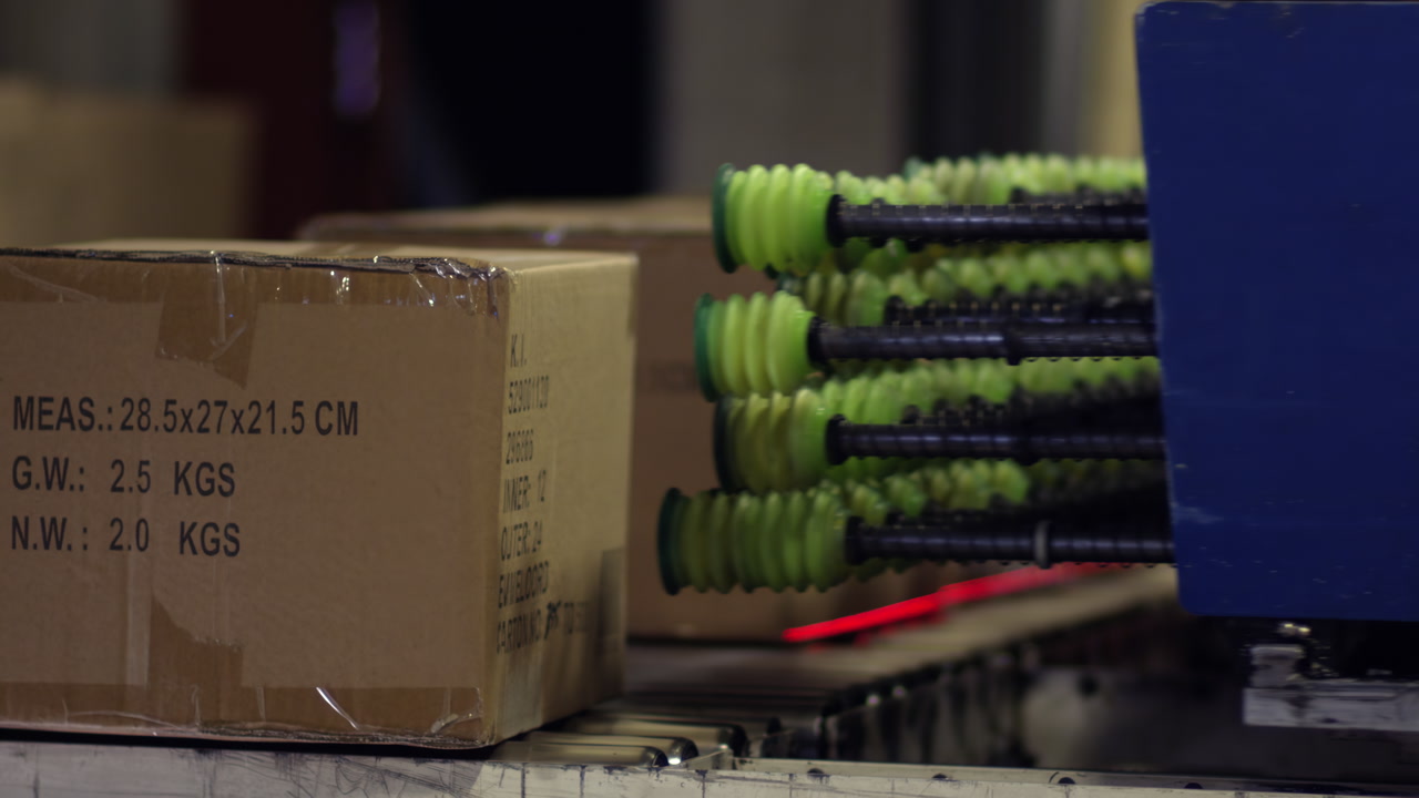 Automated conveyor belt moves cardboard boxes and green-handled products in an indoor industrial packaging and shipping facility.