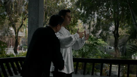 Two men practicing Tai Chi or Qigong in a traditional garden pavilion