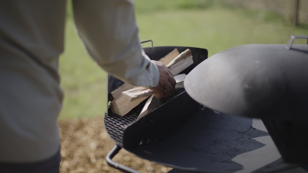 Person Putting Wood on a BBQ Grill