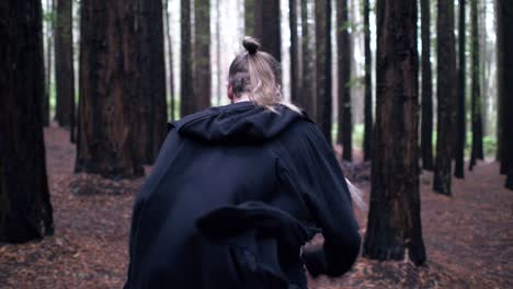 person wearing black jacket running in the woods with tall trees