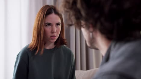 over the shoulder close up an angry brunette girl in a green jacket hits her boyfriend on the cheek with her palm during a difficult conversation and argument about life and relationships at home