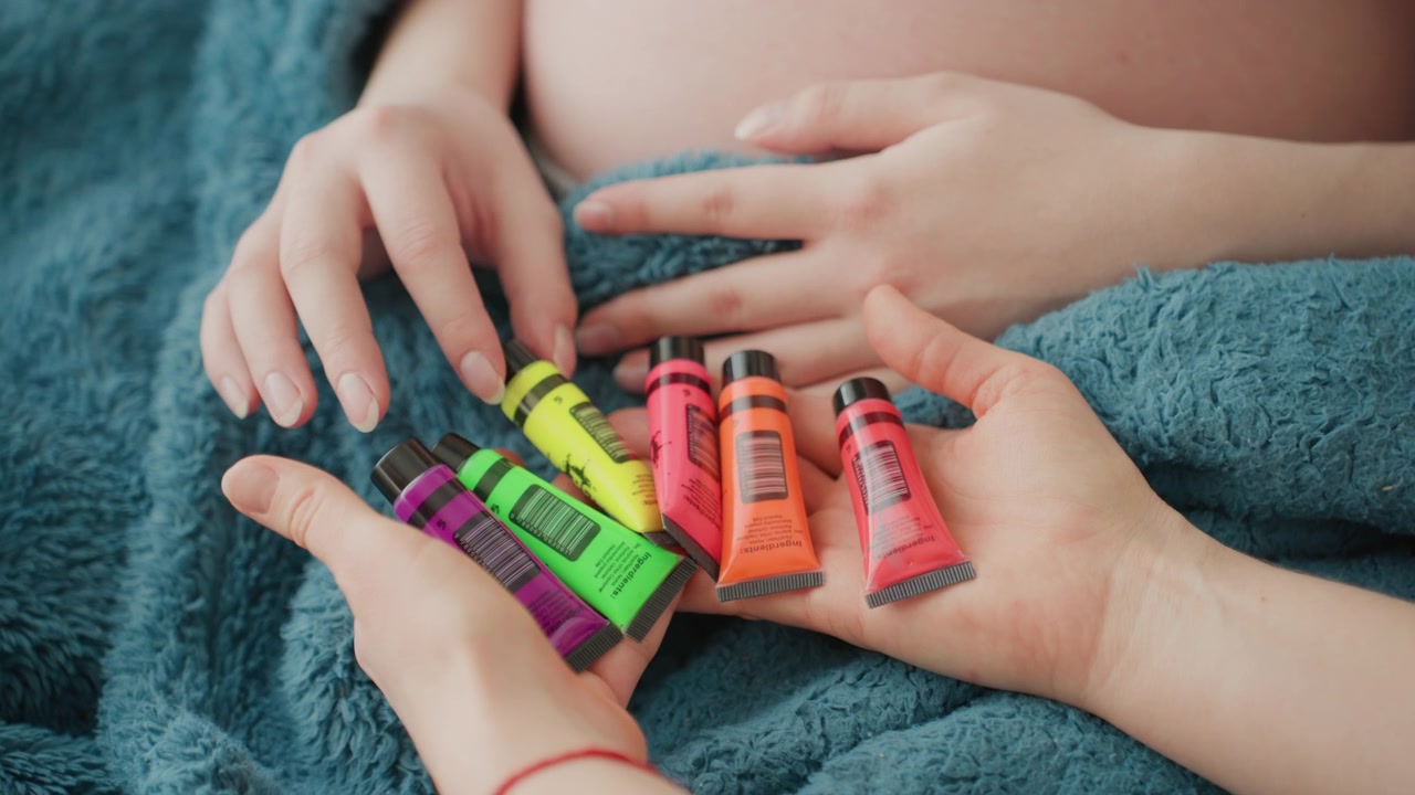 Manos sosteniendo tubos de pintura corporal coloridos para vientre de embarazada