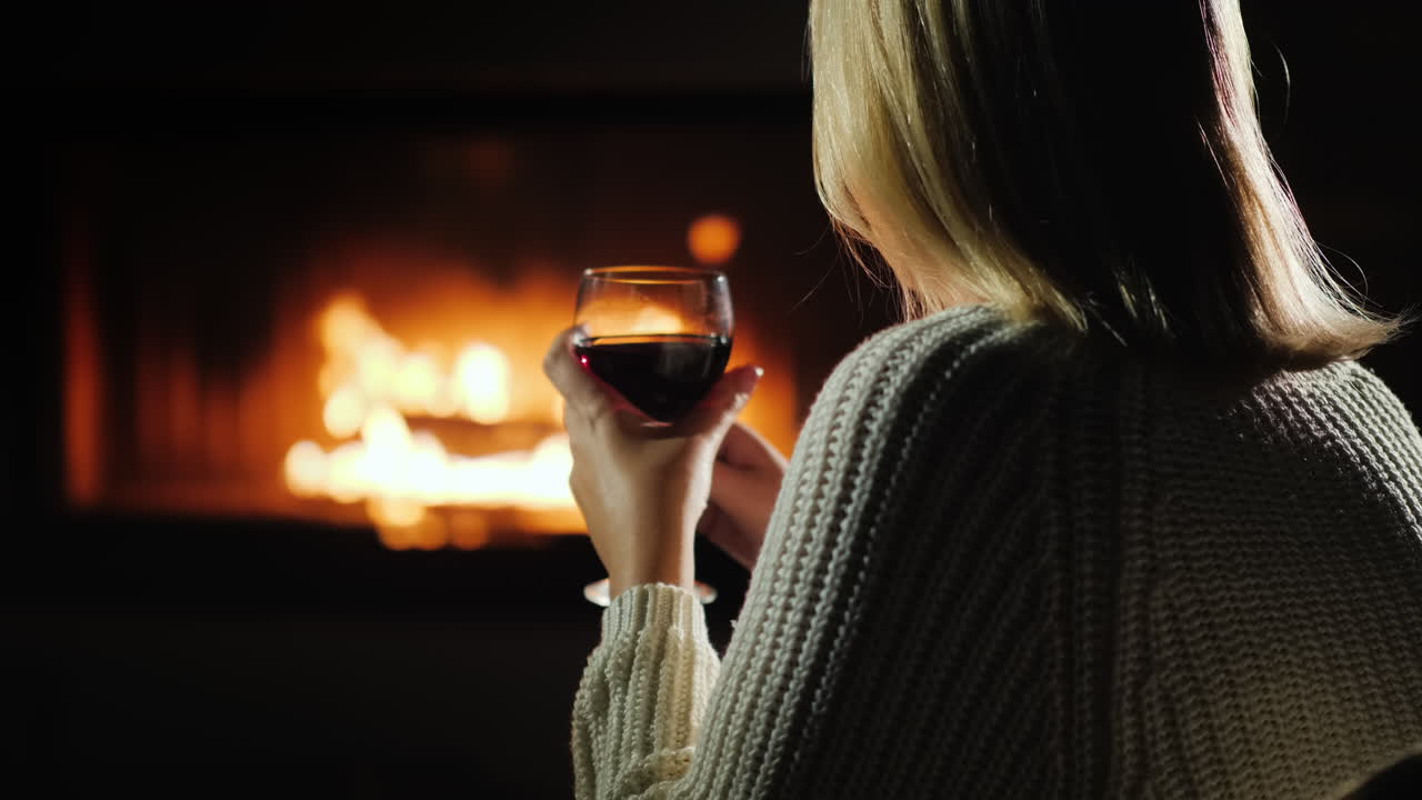 mujer bebiendo vino tinto mientras se sienta junto a la chimenea vista trasera