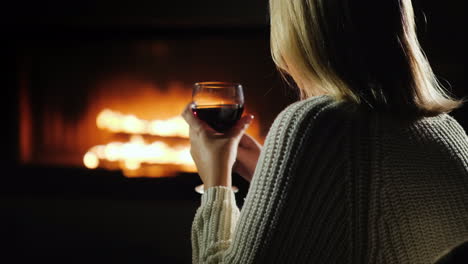 Mujer-Bebiendo-Vino-Tinto-Mientras-Está-Sentado-Junto-A-La-Chimenea-Vista-Trasera