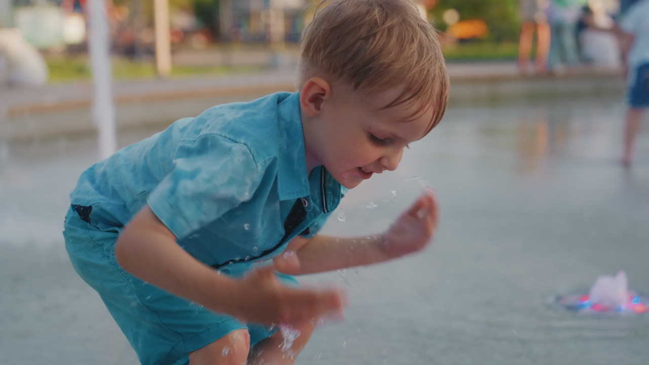 Niño jugando con las luces de la fuente en el parque el fin de semana, niño descalzo se agacha para tocar los coloridos chorros de agua LED, salpicando y riendo durante una tarde de verano, primeros planos espontáneos capturan la curiosidad, juguetón.